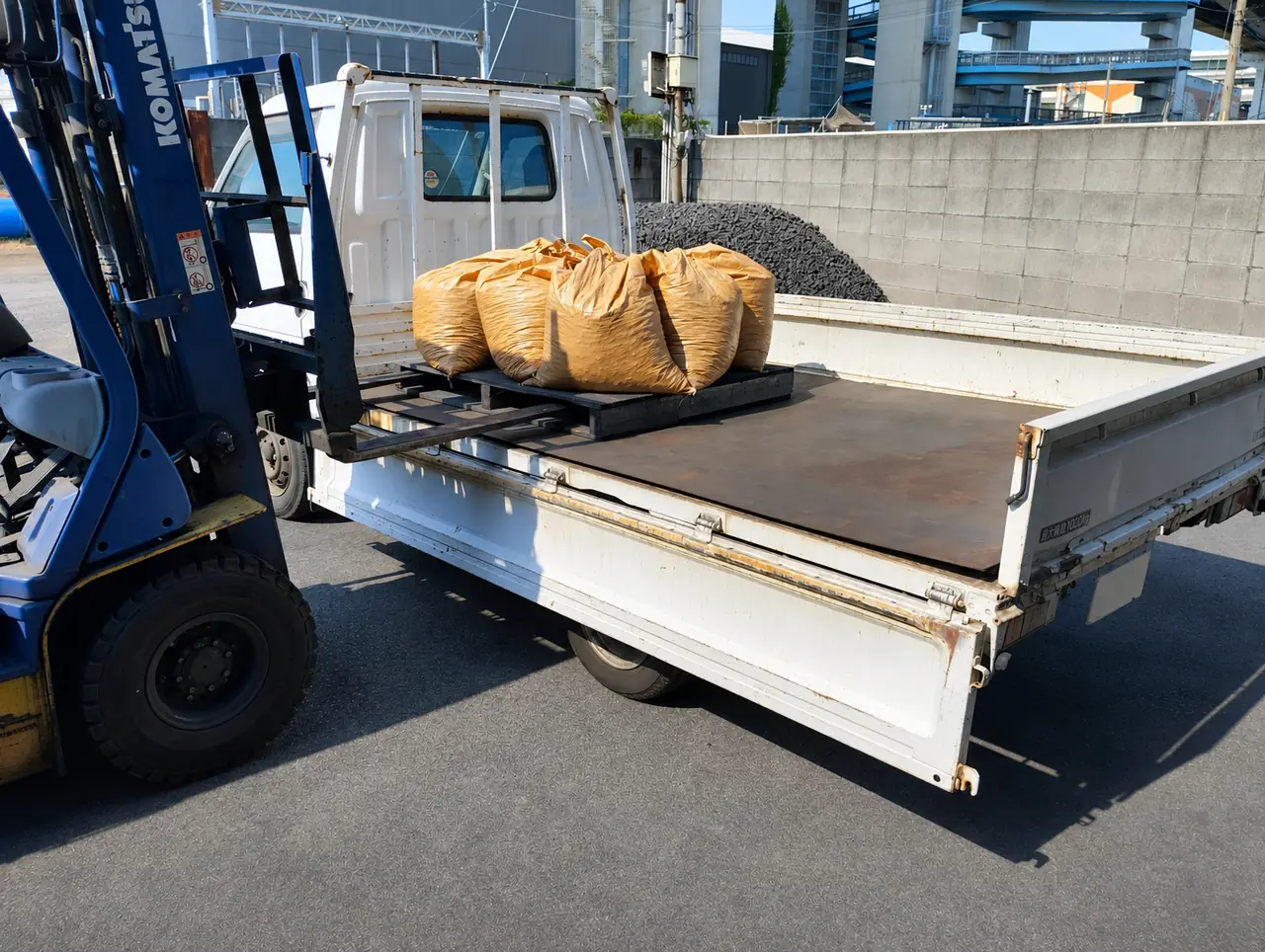 フォークリフトでコークス袋をトラックへ積み込む日新鉱産商会の作業風景